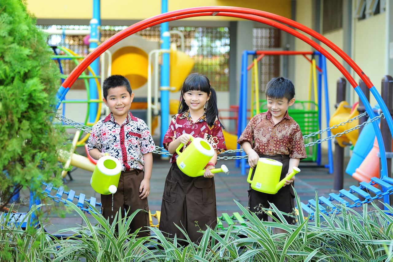 Smiling children watering plants playfully at a colorful playground in Jakarta.